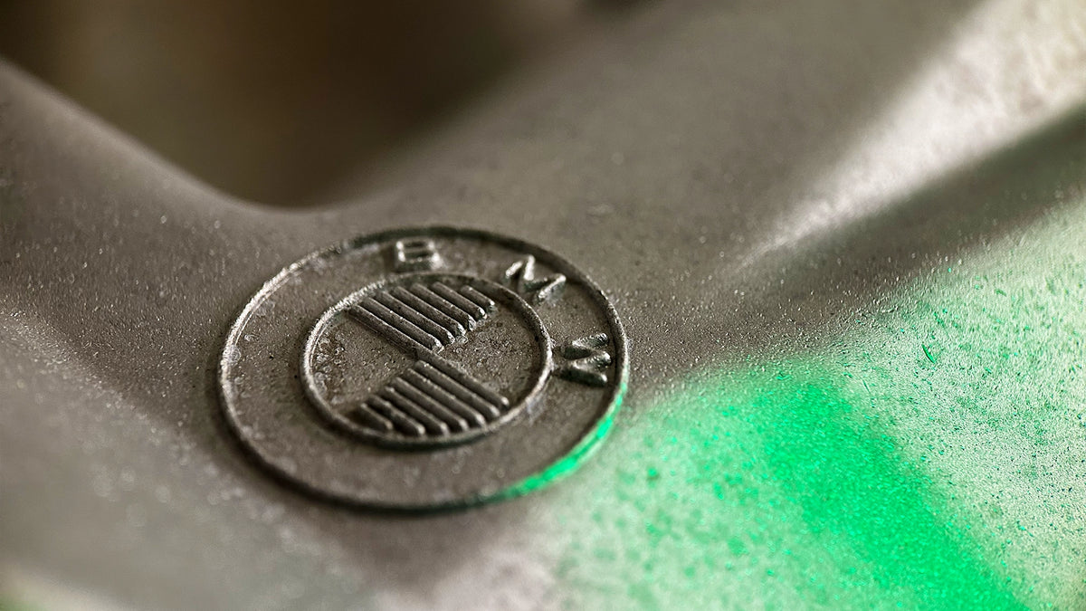 Makroaufnahme eines geprägten BMW-Logos auf einer sauberen, Vapor-gestrahlten Aluminiumoberfläche von ecoBlast. Das feine, porenfreie Finish zeigt die Qualität der Nassstrahltechnik. Die moderne grüne Beleuchtung unterstreicht die Präzisionstechnik.