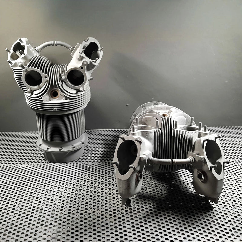 Zwei fachmännisch entlackte und gereinigte Zylinderköpfe eines Motors nach der Oberflächenbehandlung durch die Firma ecoBlast in Nettetal. Die Bauteile stehen auf einem Lochblech und weisen eine gleichmäßige, matte Metalloberfläche auf, bei der selbst die feinen Kühlrippen perfekt gesäubert wurden.