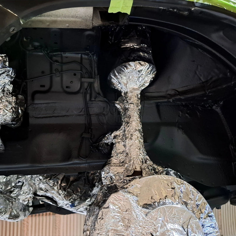 Ansicht eines frisch versiegelten Radhauses durch die Firma ecoBlast in Nettetal. Die Aufnahme zeigt den glänzend schwarzen Unterbodenschutz, während das Federbein und die Bremskomponenten zum Schutz vor dem Sprühnebel noch akkurat mit Alufolie maskiert sind.