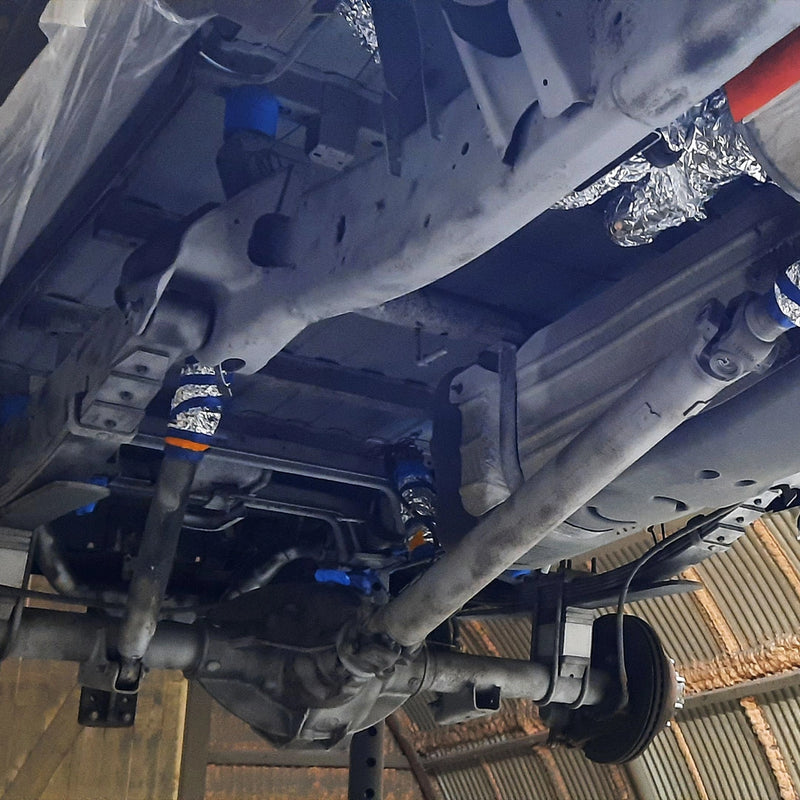 Detailansicht eines fachmännisch gereinigten Fahrzeugunterbodens bei der Firma ecoBlast in Nettetal. Das Foto zeigt den entlackten Chassis-Rahmen und Antriebskomponenten im blanken Metallzustand, wobei sensible Bereiche wie Leitungen und Gelenke sorgfältig zum Schutz maskiert wurden.